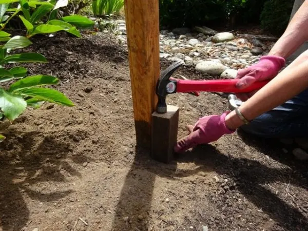Hammering a scrap of wood into the ground to help set the dirt around a fence post