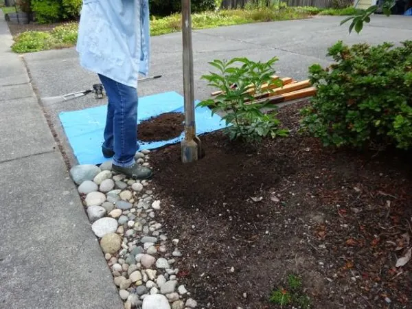 person uses a post hole digger to make hole for diy fence post