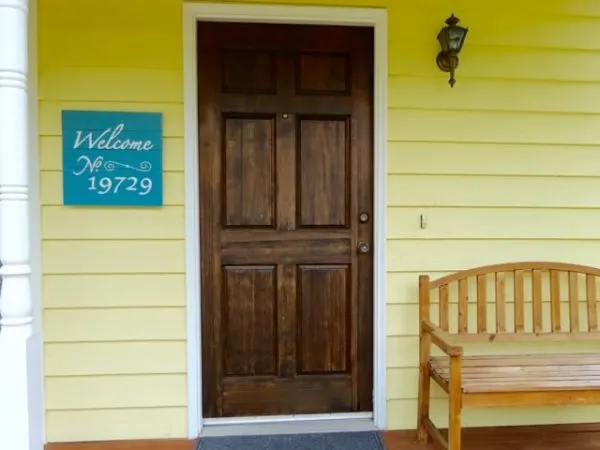 Welcome sign with address number hangs next to a front door