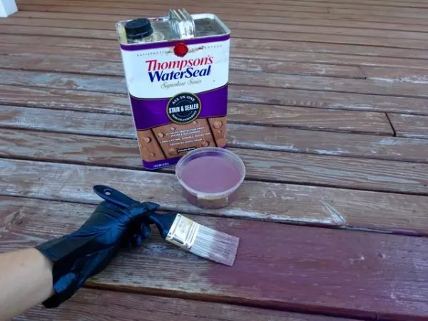 Applying deck stain to boards with a paint brush.