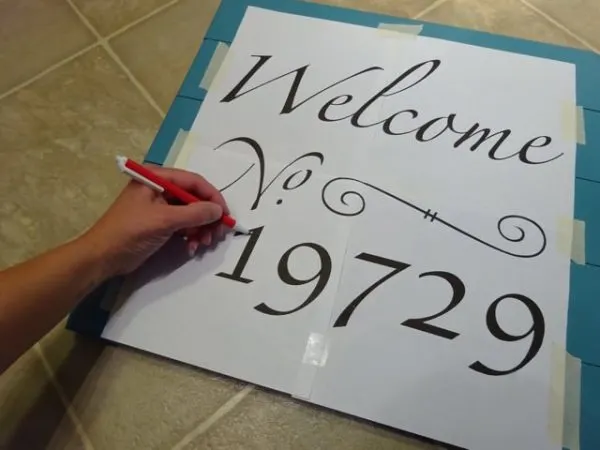 Tracing over a paper template to transfer letters to a wooden sign