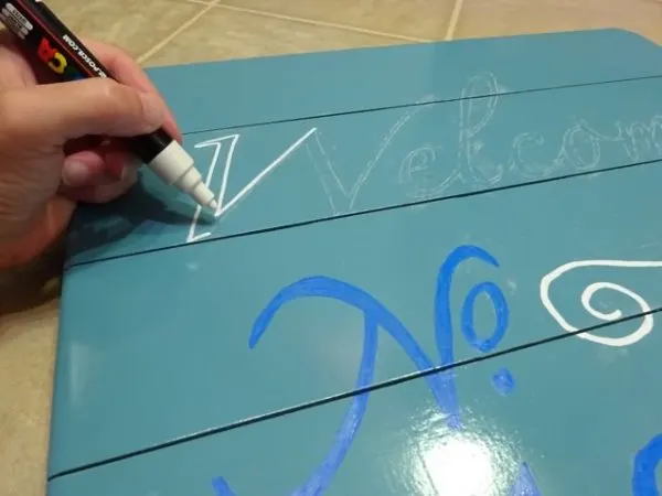 Using a paint pen to draw letters onto a hand painted sign