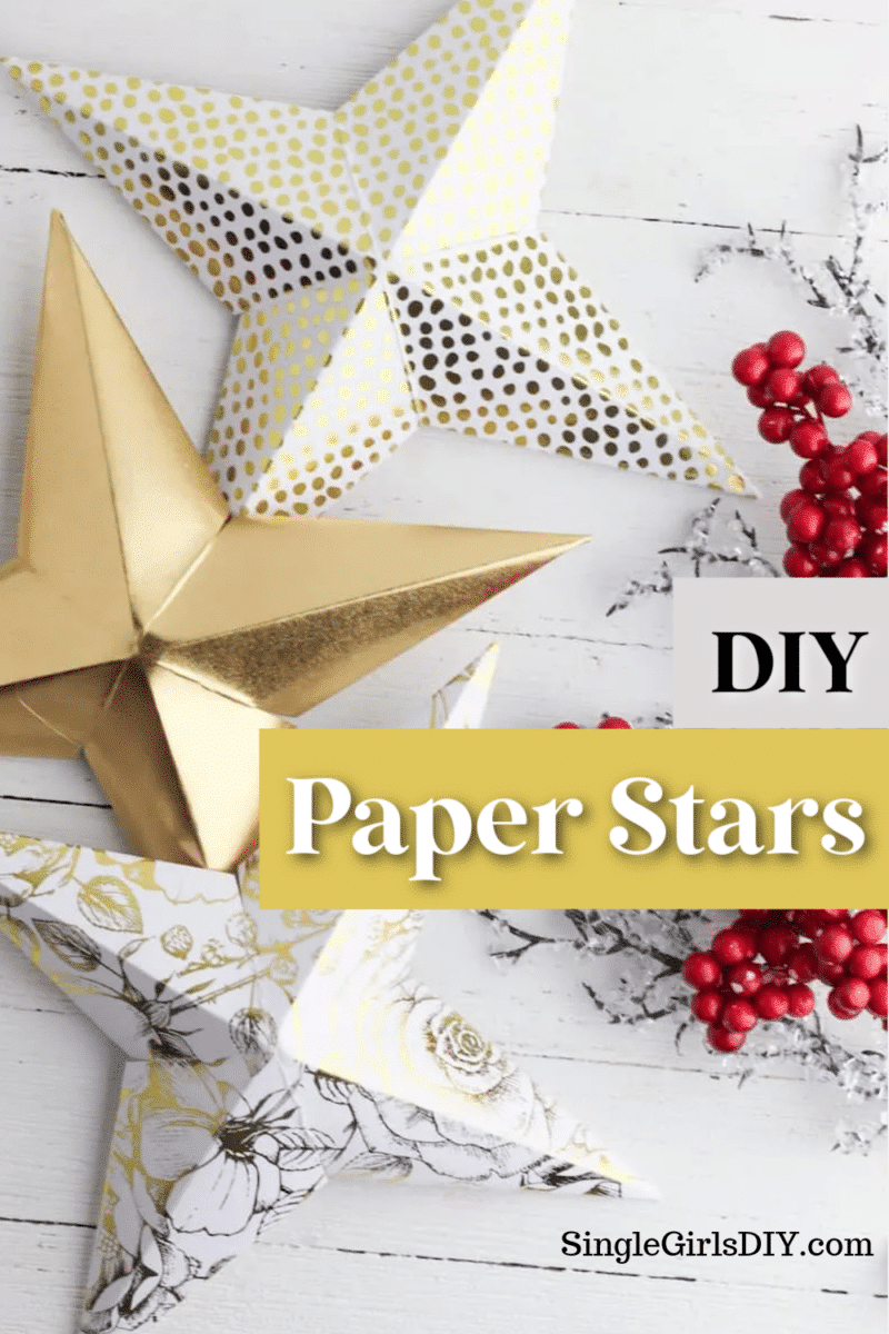 Three folded paper stars made of gold, white with gold dots, and white with black floral print paper. Red berries are scattered nearby. The text reads "DIY Paper Stars" and "SingleGirlsDIY.com.