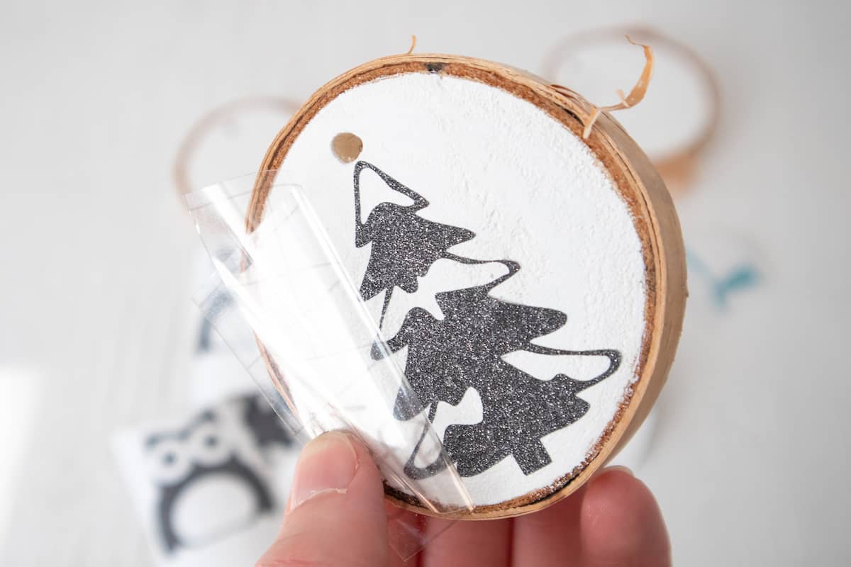 peeling away cricut transfer tape from vinyl on wood slice ornament