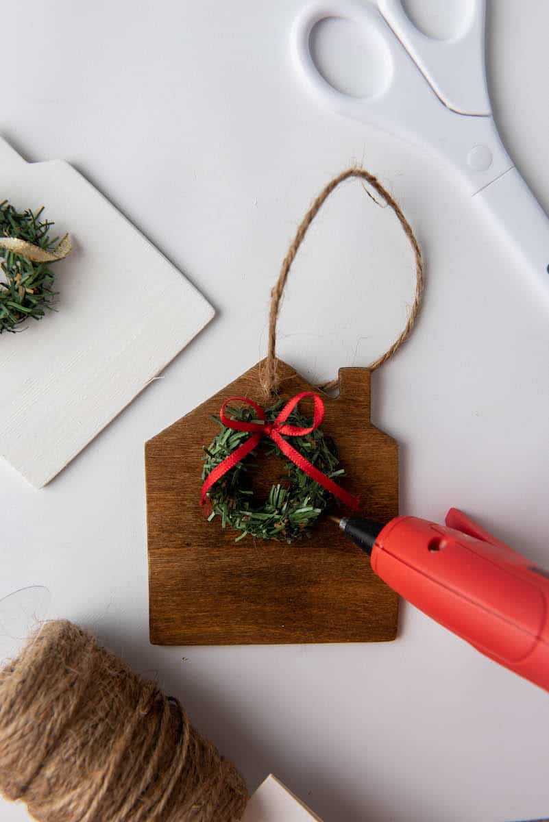 hot glueing miniature wreath to wooden house ornament