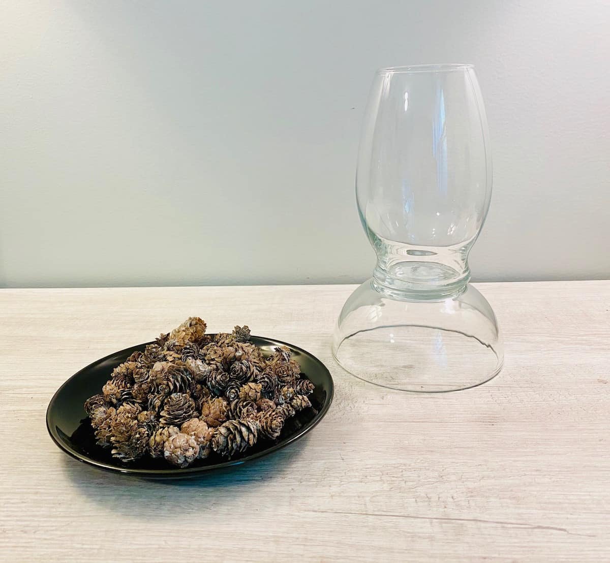 black plate of pinecones with glass hurricane lamp in background