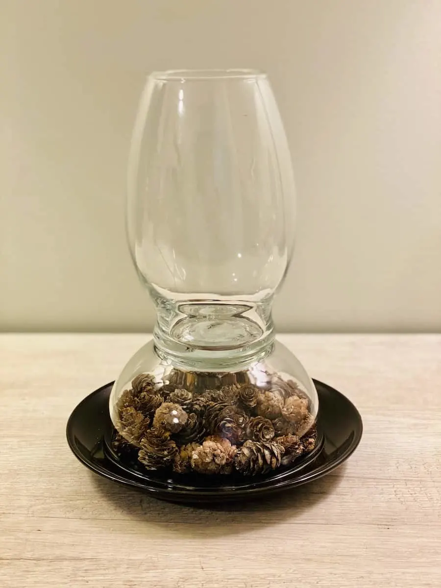 DIY Hurricane glass Lamp over black plate filled with Pinecones