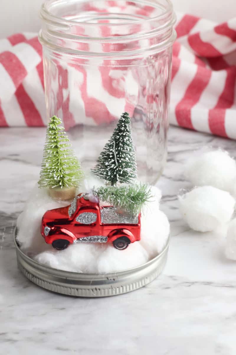 red truck ornament and trees on top of cotton balls on mason jar lid