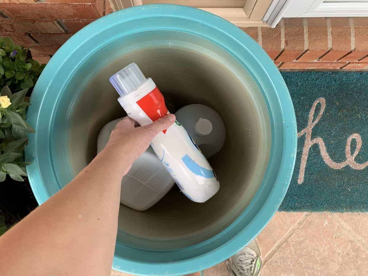 woman's hand adding plastic bottle into large flower container