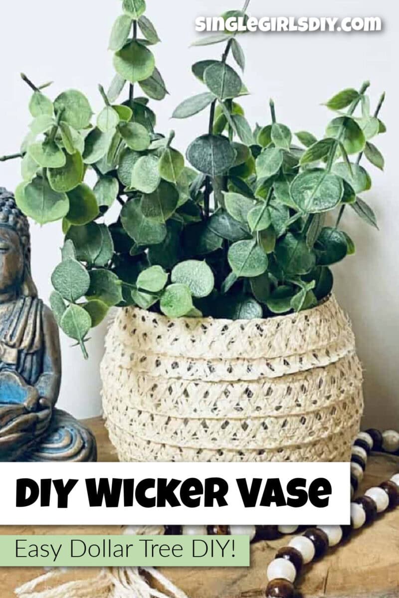 A wicker vase with faux greenery sits on a wooden surface next to a Buddha statue, a sun hat, and a beaded garland. Text reads "DIY Wicker Vase. Easy Dollar Tree DIY!.