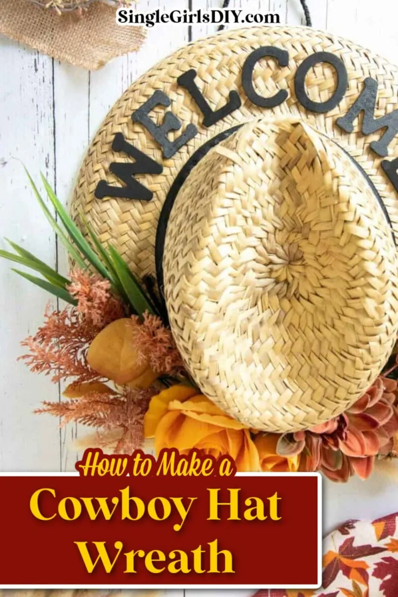 A charming cowboy hat wreath features a straw cowboy hat atop a round "WELCOME" wreath, adorned with artificial flowers and greenery, all beautifully displayed on a white wooden surface.