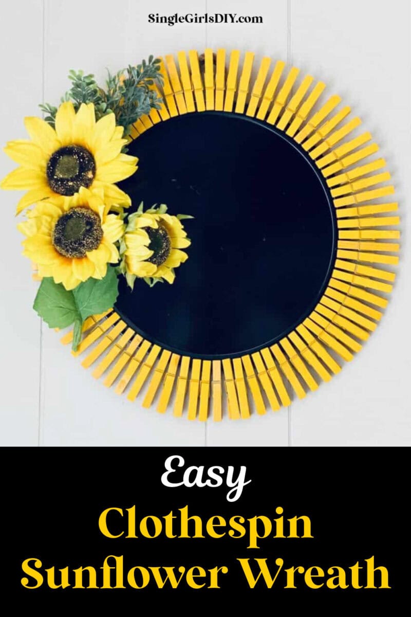 A round black base is bordered with yellow clothespins and decorated with three artificial sunflowers and green leaves on the left side, creating a charming sunflower clothespin wreath. Text reads &ldquo;Easy Clothespin Sunflower Wreath.&rdquo;.