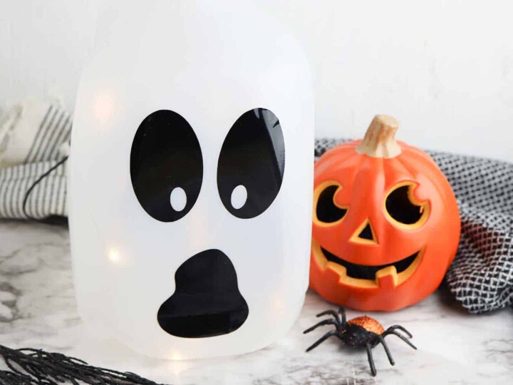 easy to make milk jug ghost luminary in front of Halloween pumpkin