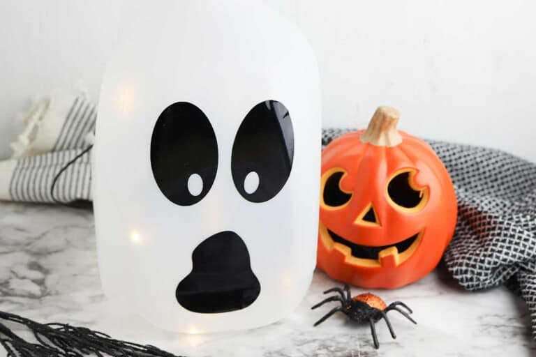 easy to make milk jug ghost luminary in front of Halloween pumpkin