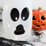 black ghost face on clear milk jug bottle with Halloween pumpkin nearby
