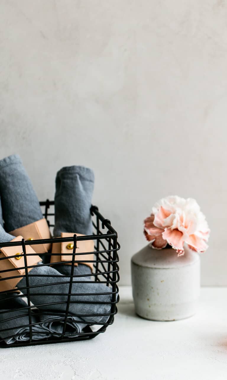 black wire basket filled with rolled napkins and a pink flower in a vase nearby