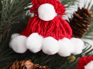 Santa hat made from red yarn and decorated with white Pom Poms lying on a Christmas tree branch