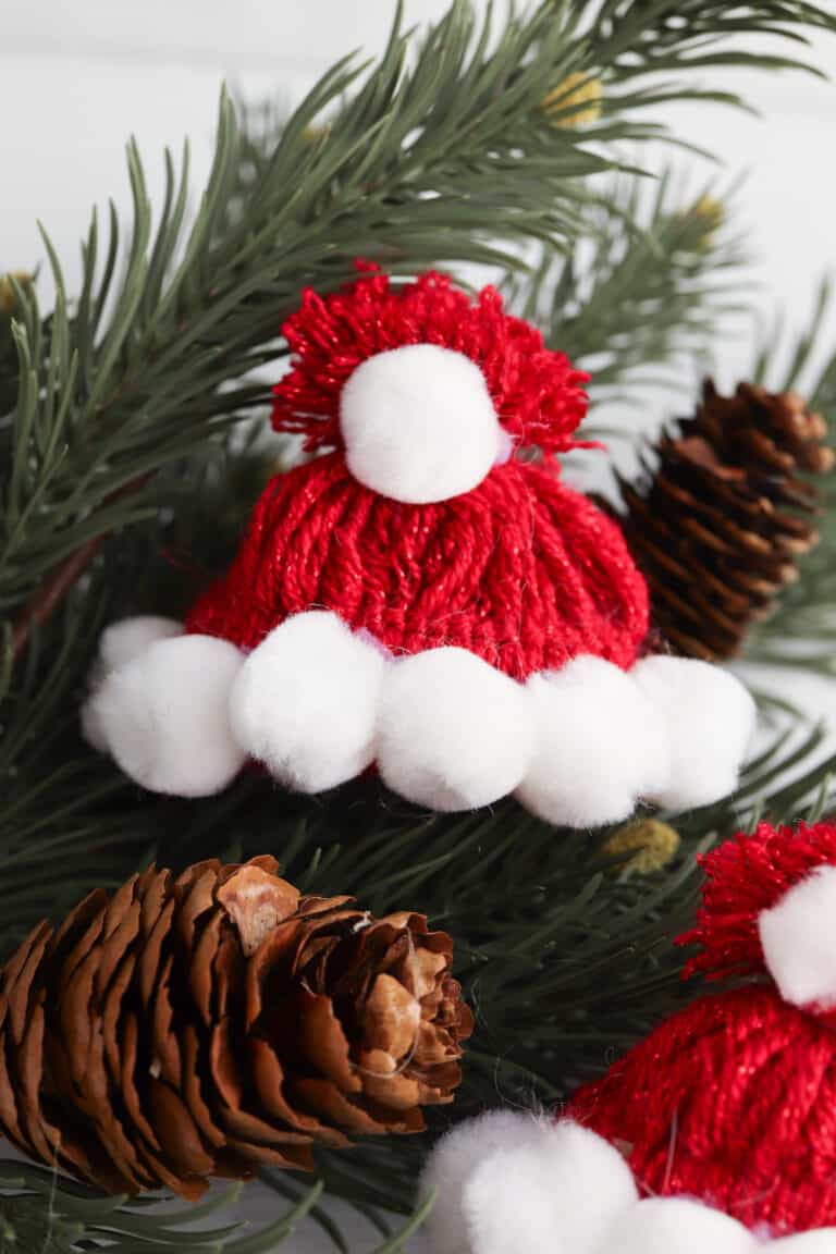 Santa hat made from red yarn and decorated with white Pom Poms lying on a Christmas tree branch