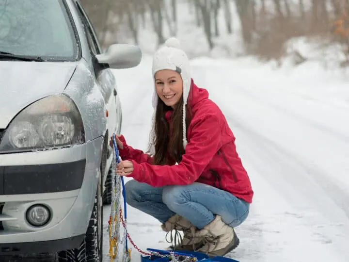 girl applying a snow chain to car tires