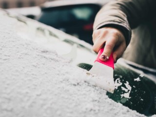 woman removing snow from windshield with ice scraper