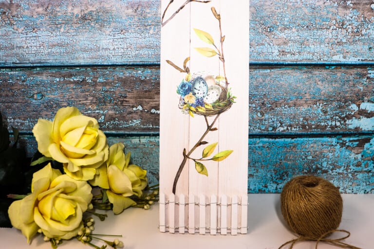 spring garden picket fence sign against a weathered blue wood background and yellow flowers nearby