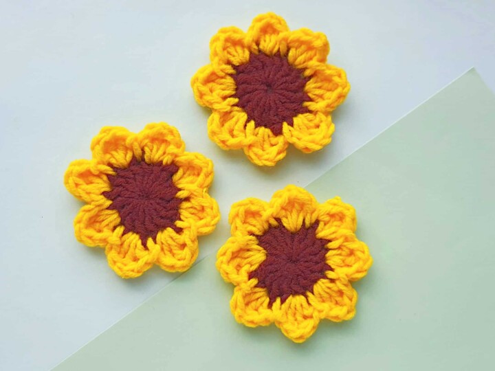 three crocheted sunflowers laying on green background