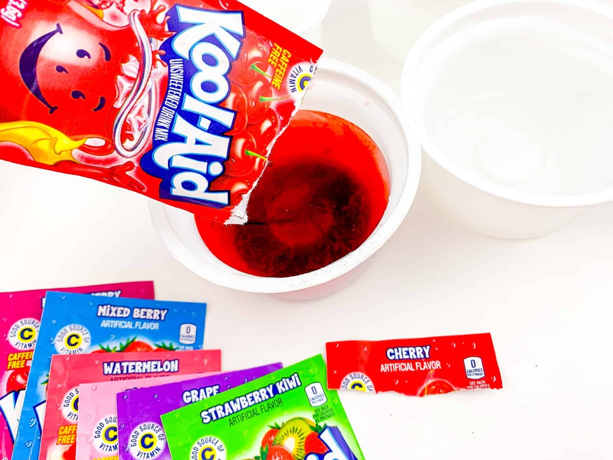 pouring kool aid drink mix into cup to dye eggs