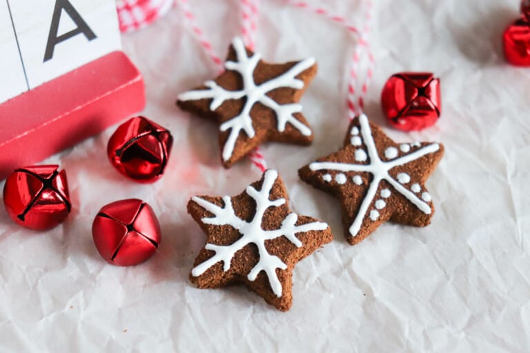 star ornaments made out of applesauce and cinnamon laying on white paper background next to red jingle bells
