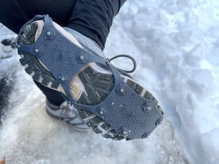 removable ice cleats worn over woman's sneaker shown against layer of snow