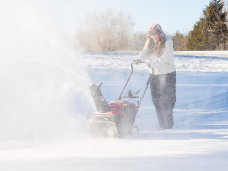 woman using a snowblower on a snow-covered driveway