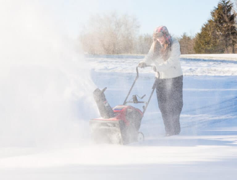 woman using a snowblower on a snow-covered driveway