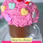 diy fake hot chocolate mug topped with pink whipped cream decorated with candy hearts and a red and white straw displayed on a china plate on top of a weathered wood table with candy hearts