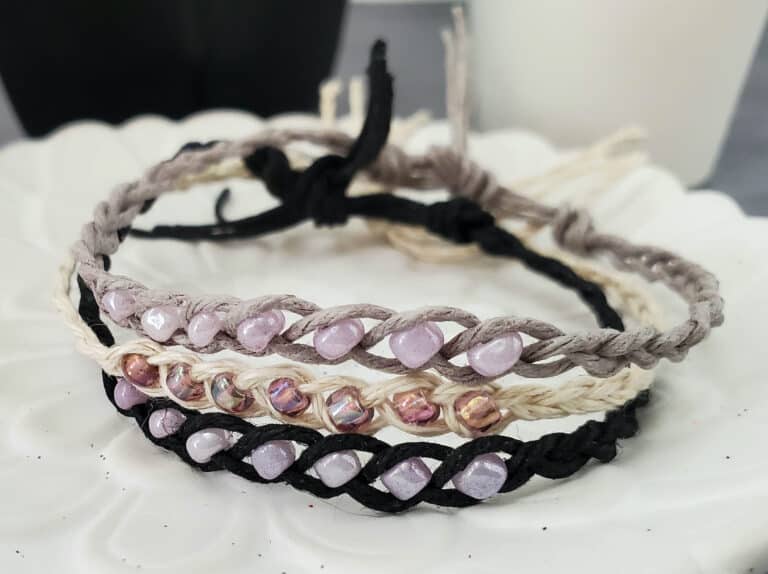 three wish bracelets made of hemp cord and beads stacked on top of each other on a white ceramic dish