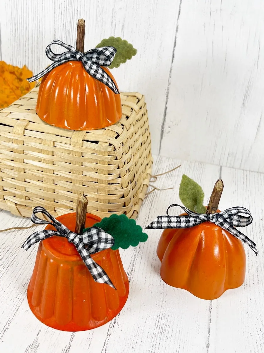Tin Mold Pumpkins with black checkered ribbon atop White Wood Background