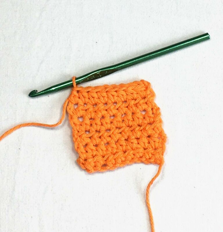 orange yarn and a green crochet hook working a half double stitch against a white background