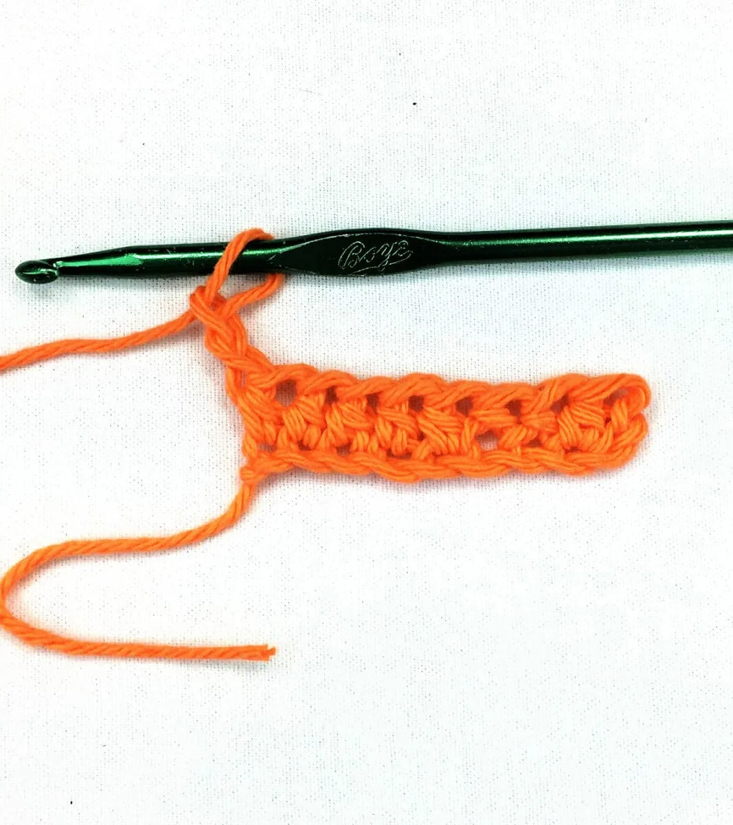 orange yarn and a green crochet hook working a half double stitch against a white background