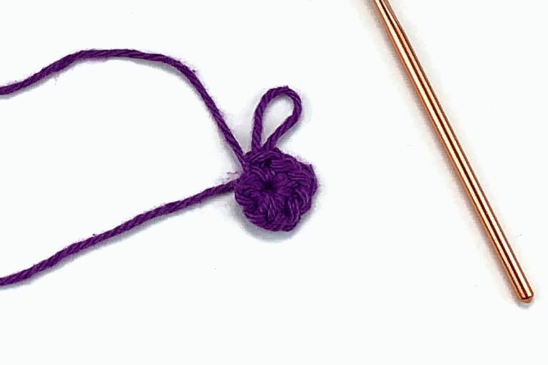 purple yarn and a gold crochet hook working a magic ring crochet stitch against a white background