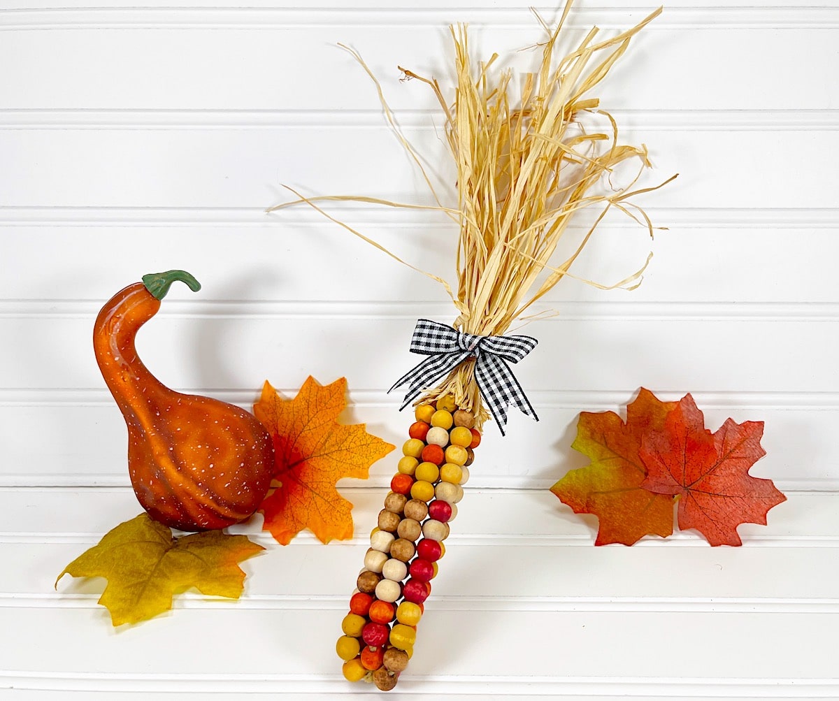 Bead Corn stalk with fall leaves on a white wood background