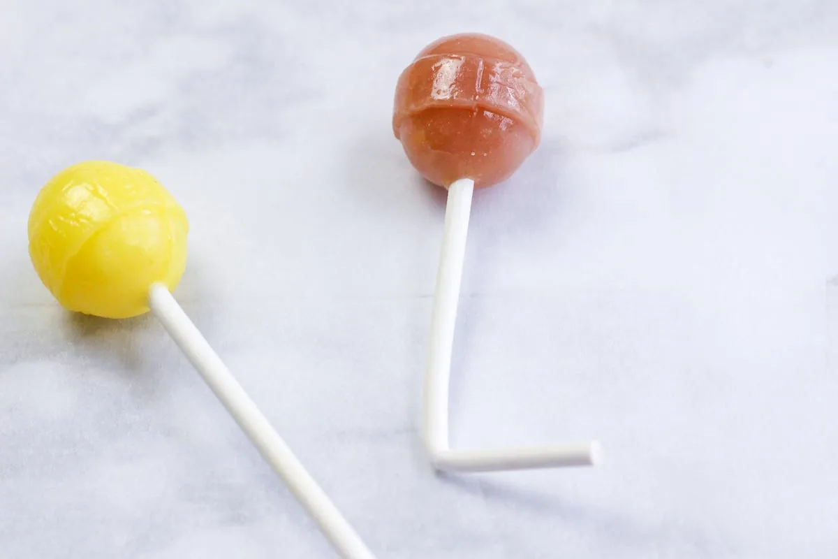 Candy Nativity Step 11 Two yellow and orange lollipops on a white surface.