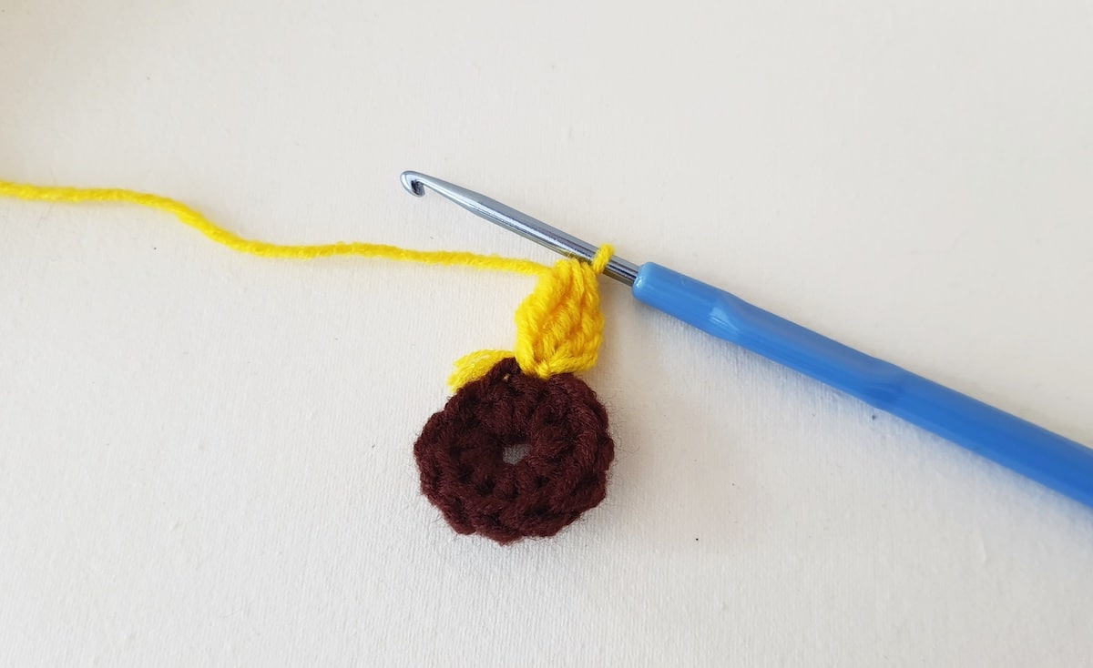 Crochet Sunflower Granny Square Step 11 A crocheted donut with a yellow yarn and a yellow crochet hook.