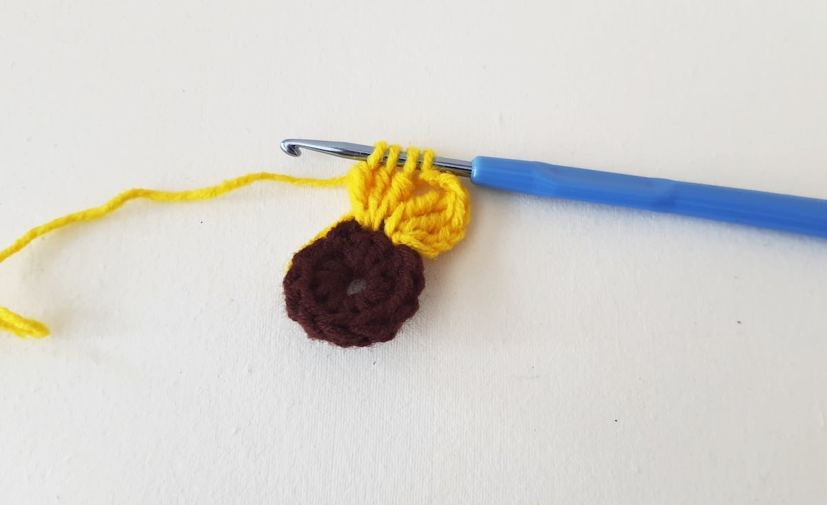 Crochet Sunflower Granny Square Step 13 A crochet hook with a yellow and brown yarn.