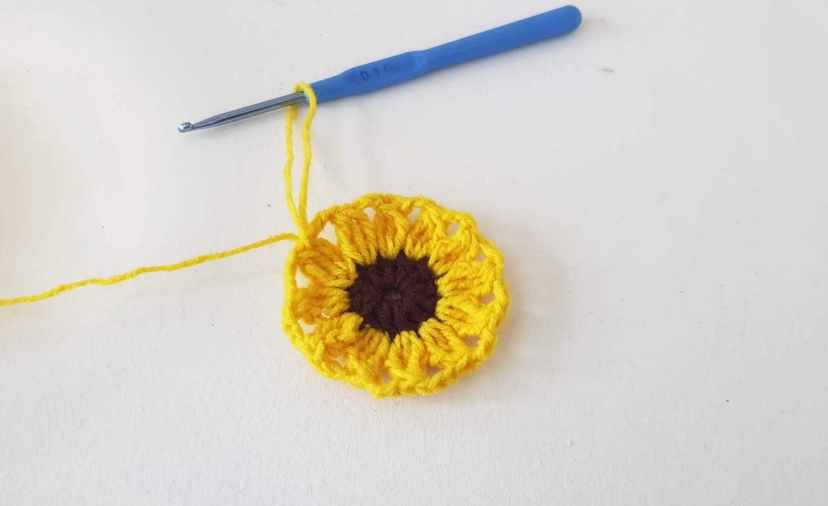 Crochet Sunflower Granny Square Step 17 A yellow crochet flower with a blue crochet hook.