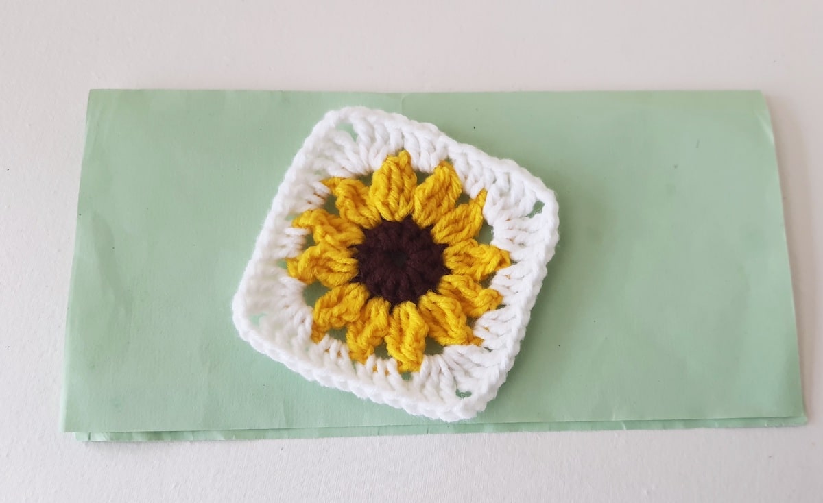 Crochet Sunflower Granny Square Step 27 A crocheted sunflower on a green piece of paper.
