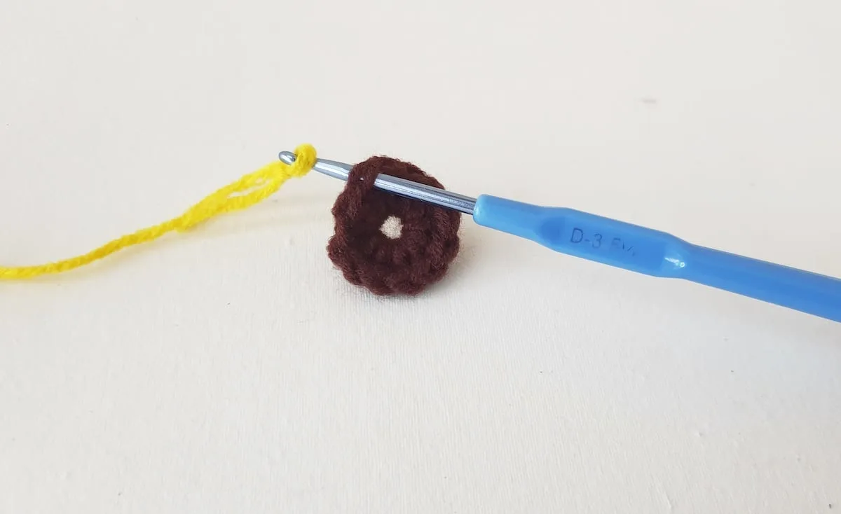 Crochet Sunflower Granny Square Step 6 A crocheted donut with a blue crochet hook.