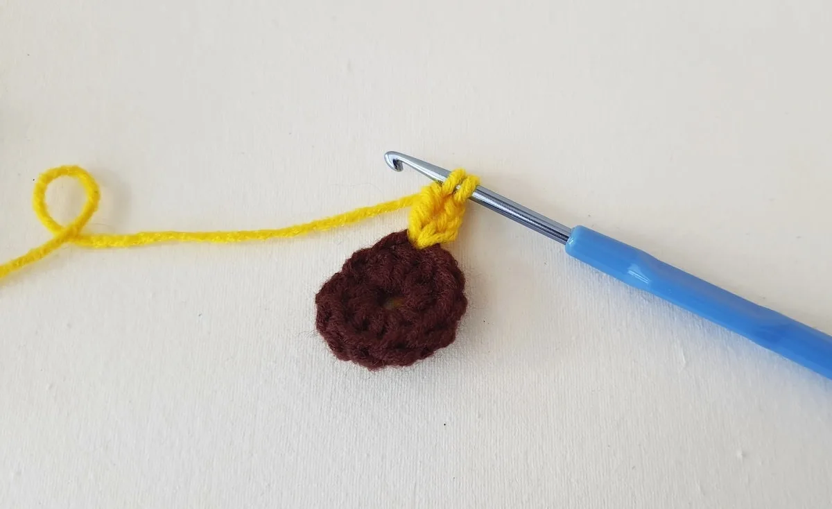 Crochet Sunflower Granny Square Step 9 A brown crocheted flower with a blue crochet hook.