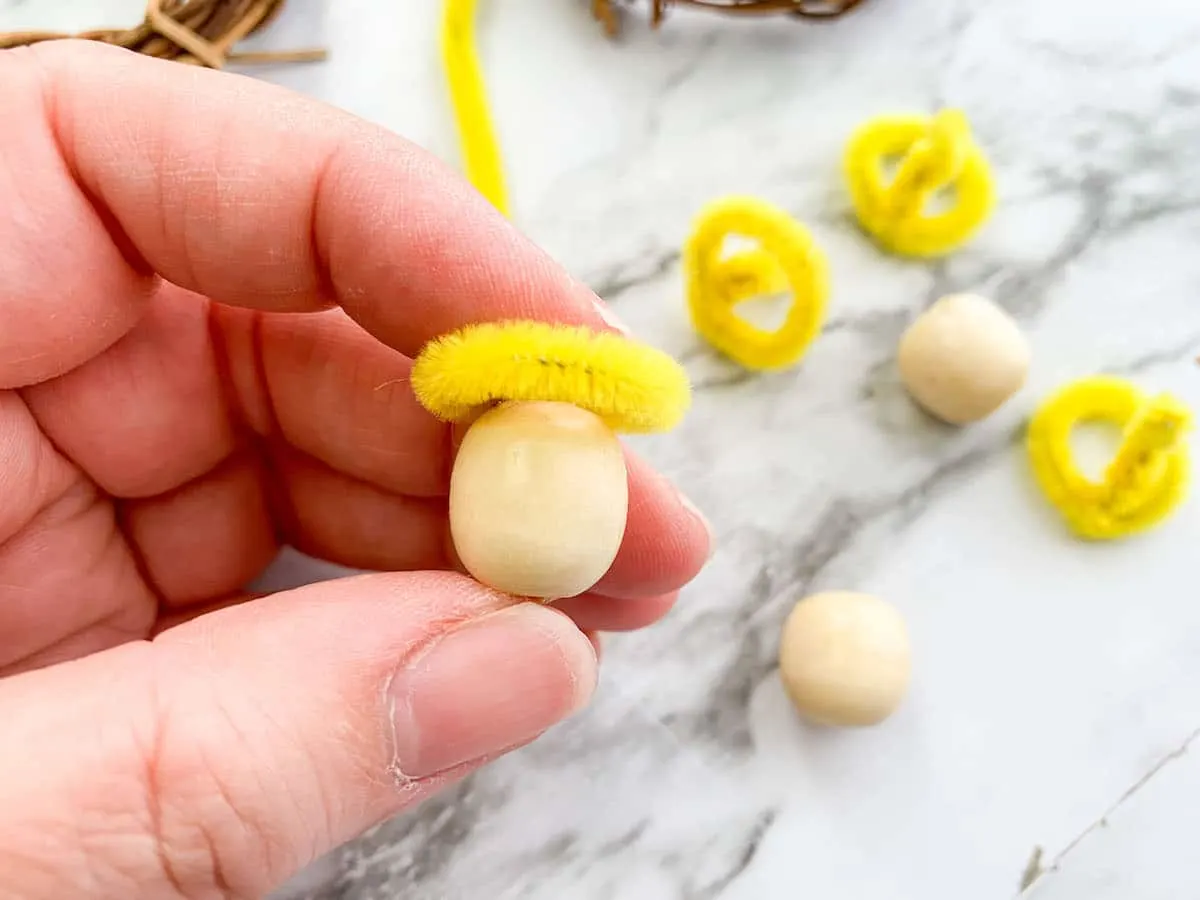 Emmanuel Wreath Step 5 A person holding a wooden egg with a yellow halo pipe cleaner.