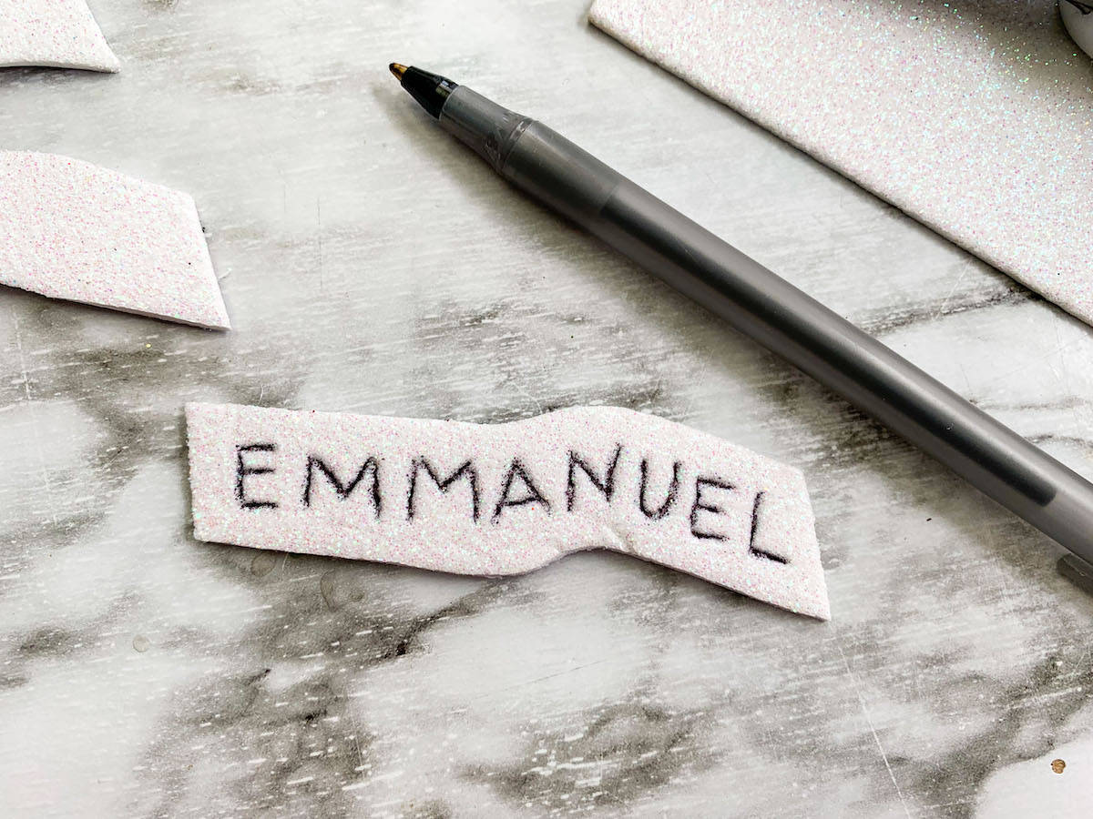 Emmanuel Wreath Step 9 The word emmanuel is written on a piece of paper next to a pen.