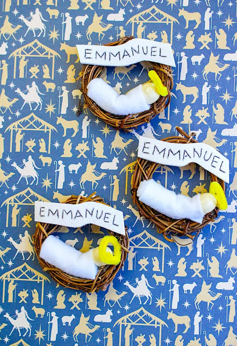 Emmanuel Wreath Three nativity ornaments on blue backdrop with white religious figures