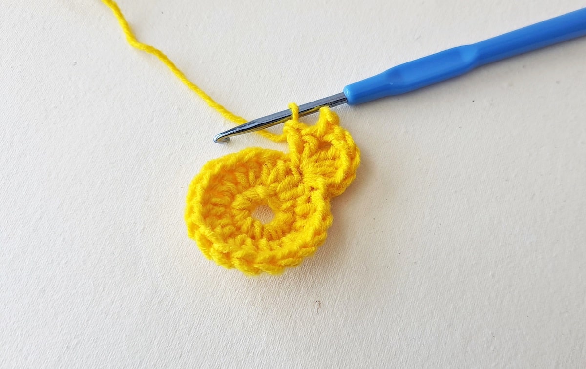 Maple Leaf Crochet Pattern Step 10 A yellow crocheted flower with a blue crochet hook.