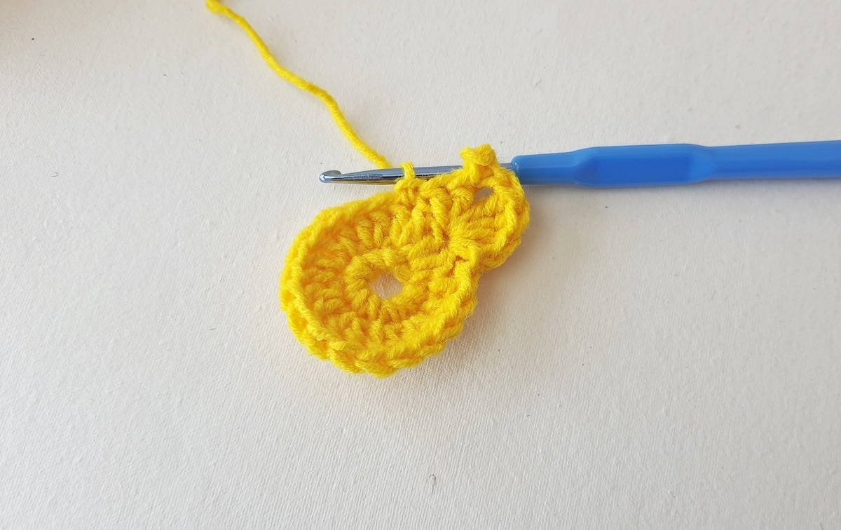 Maple Leaf Crochet Pattern Step 11 A yellow crocheted flower with a blue crochet hook.